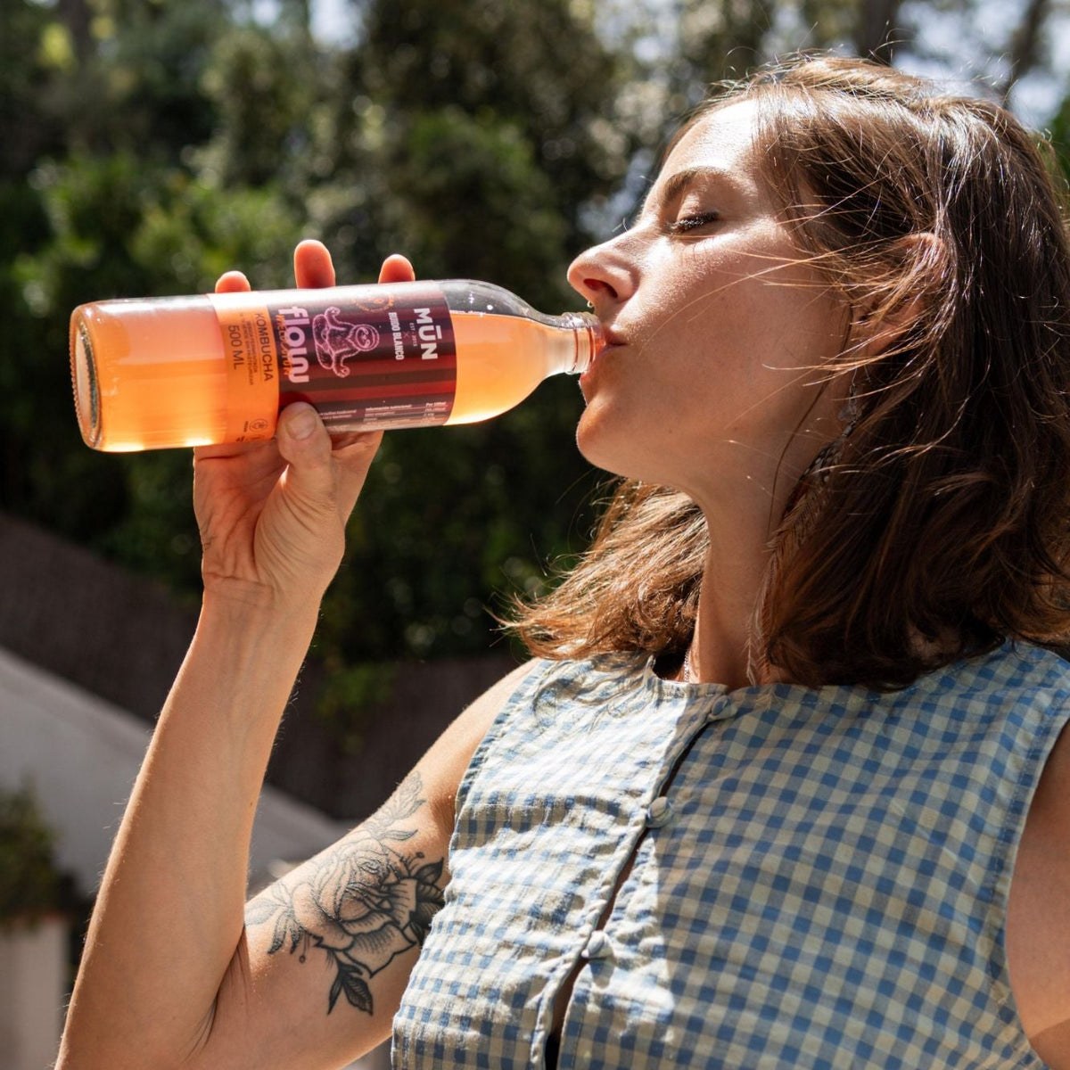 Mujer bebiendo kombucha Mūn x Ruido Blanco FLOW de la botella de 500 ml al aire libre